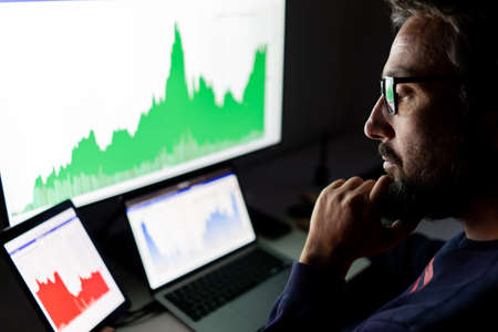 Crypto trader investor analyst looking at screen analyzing financial graph data on pc monitor, online stock exchange market ,over shoulder view.の写真素材