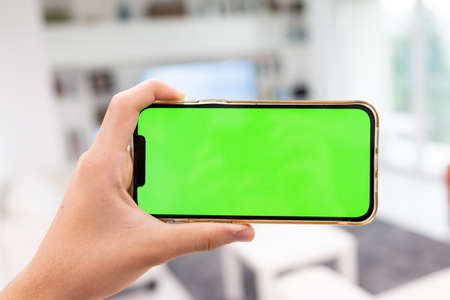 Hand in modern living room via smart home on mobile phone with blank green screen. High quality photoの写真素材