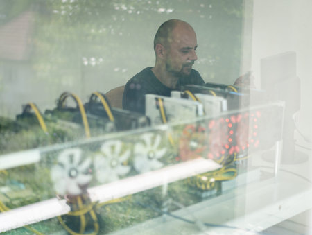 Young programmer adjusting cryptocurrency mining rig to optimal operational settings. High quality...