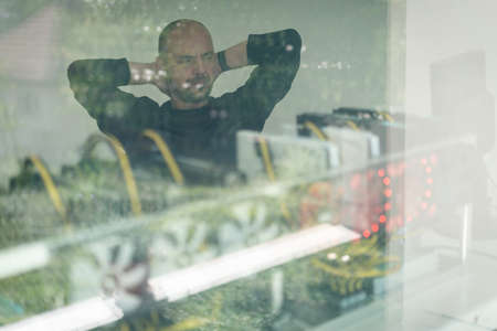 Young programmer adjusting cryptocurrency mining rig to optimal operational settings. High quality photoの写真素材