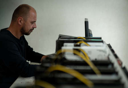 Young programmer adjusting cryptocurrency mining rig to optimal operational settings. High quality photoの写真素材