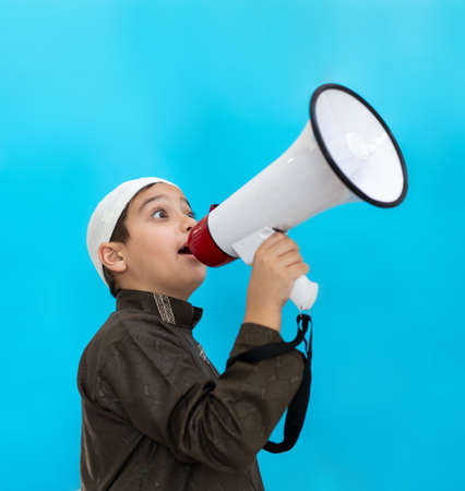 Muslim child in white traditional clothes, saying message on megaphone. High quality photoの写真素材