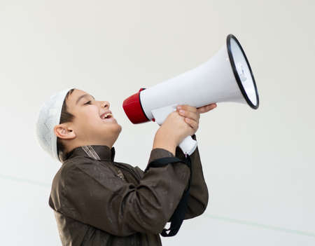 Muslim child in white traditional clothes, saying message on megaphone. High quality photoの写真素材