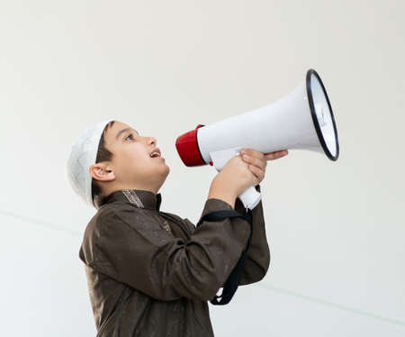 Muslim child in white traditional clothes, saying message on megaphone. High quality photoの写真素材