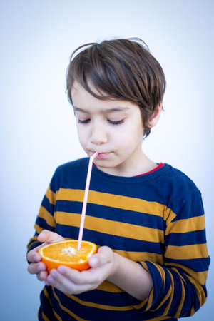 Little cute boy taking juice out of orangeの写真素材
