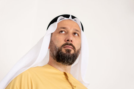 Close up portrait of man wearing traditional arabic clothing, standing against white background....