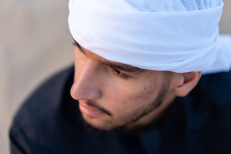 Arab man sitting on sand in the desert during golden hour, wearing traditional arab clothing. High quality photoの写真素材