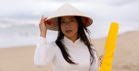 Portrait of thai woman at the beach wearing traditional conical hat and holding hand fan. High quality photoの写真素材