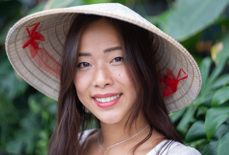 Portrait of viatnamese woman wearing traditional conical hat, standing in front of green plants. High quality photoの写真素材