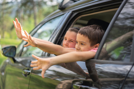Happy brother and sister reaching hands out of car window during road trip. High quality photoの写真素材