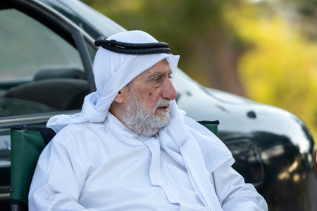 Senior arab man sitting outdoors wearing traditional arab clothing, and observing. High quality photoの写真素材
