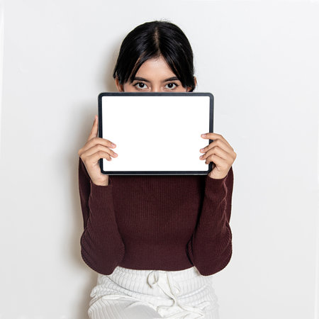 Image of a white blank screen tablet held by a woman while covering her face for mockupの写真素材