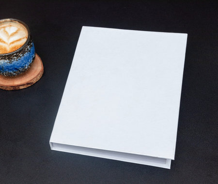 Image of a blank white hardcover book on the top of a black table for mockup