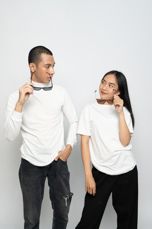 A couple wearing white blank shirt and a glasses looking at each other while holding their glasses on a white backgroundの写真素材