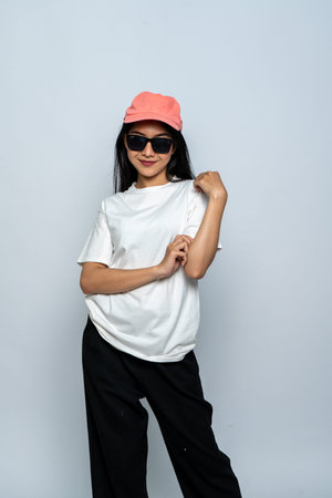 A young woman with a white blank shirt and glasses doing a cool pose while smiling with the white...