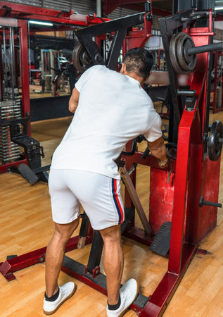 Back side of a gym athlete wearing a white blank shirt doing weight lifting at a gym, mockup image