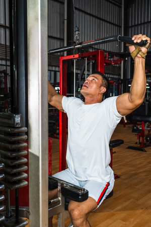 Image of a gym athlete wearing a white blank shirt doing a weight lifting while sitting down at a...