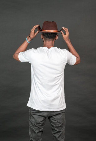 Back side image of an african man wearing white blank shirt with a hat, doing a simple pose by...