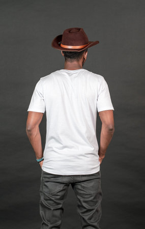 Back side of an african man with blank white shirt doing a simple pose, with black background mockup...
