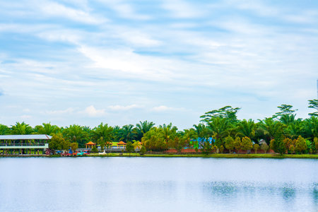 A landscape scenery with a lot of trees, a lake, and a blue sky with some visible cloud, colorful sceneryの写真素材