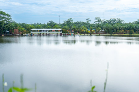 A building near a river taken from a far with a lot of trees around it, and a beautiful skyの写真素材