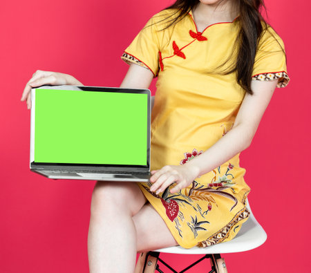 Young asian women presenting a laptop with green colored screen, isolated on a red backgroundの写真素材