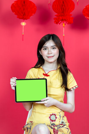 Young asian women presenting a tablet with green colored screen, isolated on a red backgroundの写真素材
