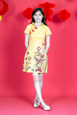A young asian woman sitting and holding a white box for mockup while wearing simple yellow chinese dress, isolated on red backgroundの写真素材