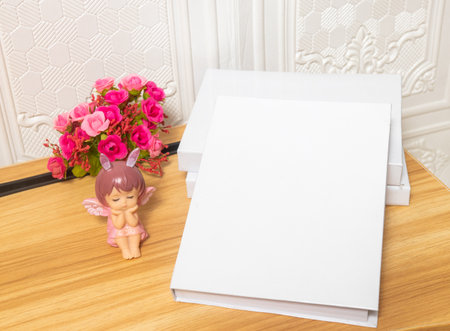 A white colored hardcover books on the top of a brown table with wooden texture and some decorations arranged around it, hardcover mockup template imageの写真素材