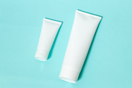 Two white colored cream bottle laying out next to each other on the top of a blue paper, bottle...