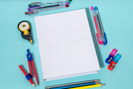 A white colored hardcover book laying out on the top of a blue paper with some stationery item placed around it, hardcover mockup template imageの写真素材