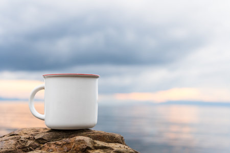 An enamel mug standing still on the top of a rock while showing the out of focus scenery at the background, enamel mug mockup imageの写真素材
