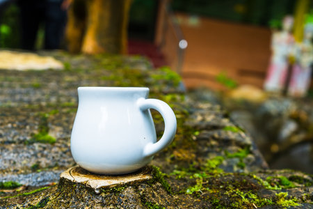 A caramel mug standing out of a top man made tree stump with out of focus building and statue as the background, caramel mug mockup imageの写真素材