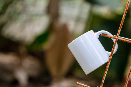 A blank white coffee mug hanging on to a rusty iron with out of focus background, coffee mug mockup imageの写真素材