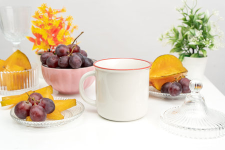 A white blank enamel mug on the top of a rounded mat with the fresh fruits arranged around it,...