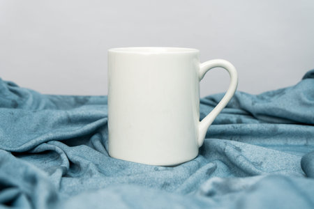 A white blank coffee mug standing out on top of a blue cloth minimalist concept, coffee mug mockup...