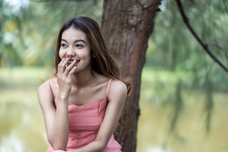 A smiling young woman in pink dress sitting in the nature, with the empty right spaceの写真素材