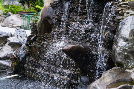 The small fountain, delicately flowing into the tranquil pond, adds an enchanting touch to any outdoor setting and creates a peaceful ambianceの写真素材