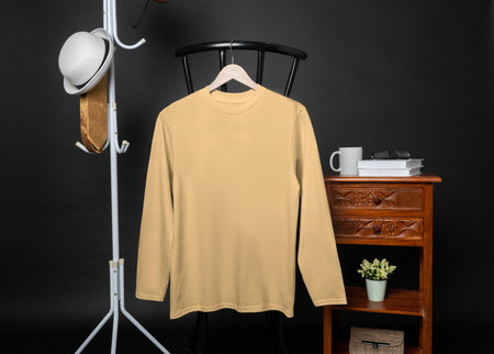 A blank light orange shirt hanged on to a chair with minimalist decorations, on a black background, shirt mockup imageの写真素材