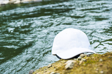 The addition of a white cap hat above a rock near the river creates a sense of style and sophistication in this peaceful and serene setting, white blank cap hat mockup imageの写真素材