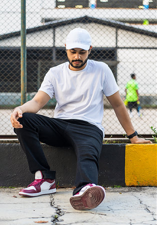 Seated young man in white shirt and cap hat with blurry tennis court, white blank cap hat and shirt mockup imageの写真素材