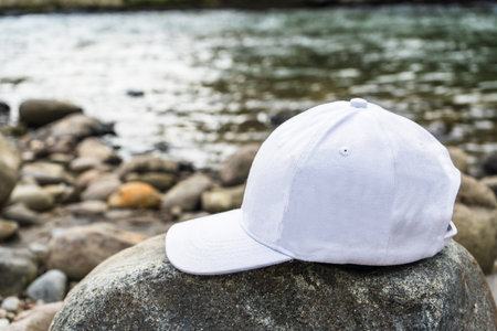 This beautiful photo captures the essence of calm and relaxation, with a white cap hat tastefully positioned above a nearby rock near the river, white blank cap hat mockup imageの写真素材