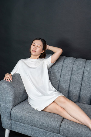 Elegant portrait of an Asian woman sitting on a minimalist sofa, shirt dress mockup template imageの写真素材
