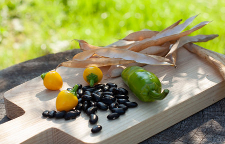 Peeled black beans. Dry beanÂ´s pods. Yellow and green chilli. Wooden cutting board
