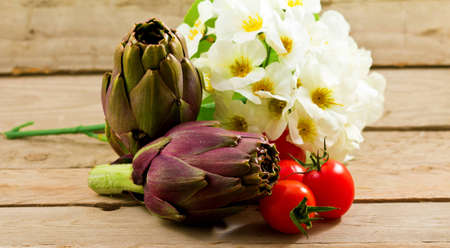 artichokes and tomatoes decorated with flowers on a wooden backgroundの写真素材
