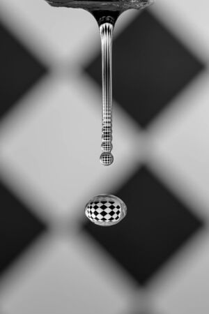 water flows from the tap in a thin stream, breaking into drops that reflect the background in a...