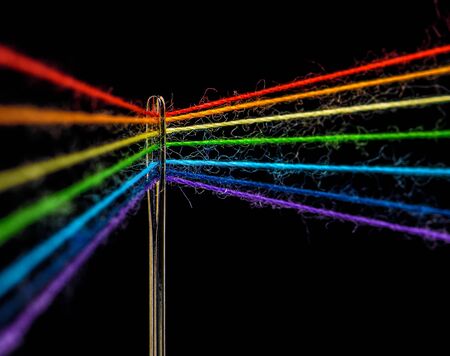 Multicolored threads, forming the colors of the rainbow, are threaded through the eye of a sewing needle, macroの写真素材
