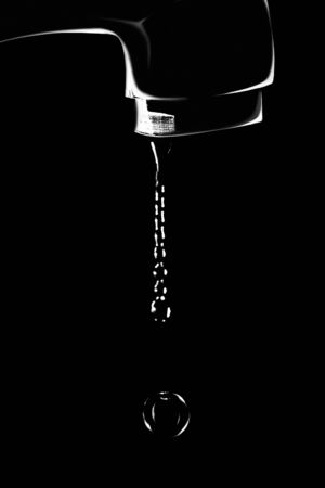 a thin trickle of water flows from the tap, breaking into drops, on a black backgroundの写真素材