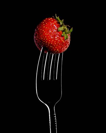 red strawberries on a fork, close-up isolated on a black backgroundの写真素材