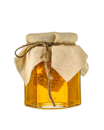 Glass open jar of honey and a spoon on it with honeycombs on a light gray background
